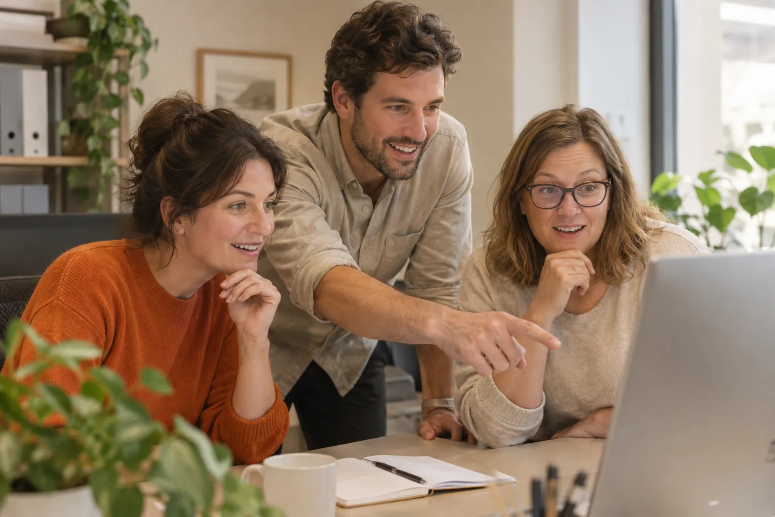 Three colleagues smiling at a laptop while one points at the screen